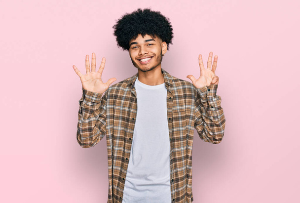Mladý africký Američan s afro vlasy na sobě ležérní oblečení ukazuje a ukazuje prsty číslo devět a zároveň se usmívá sebevědomě a šťastně.  - Fotografie, Obrázek