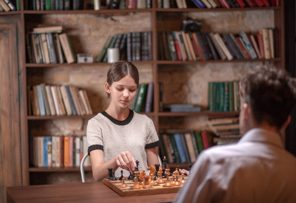 A boy and a girl play chess, teenagers play a board game, sports interest, schoolchildren are sitting at the table, learning to play chess. - Photo, Image
