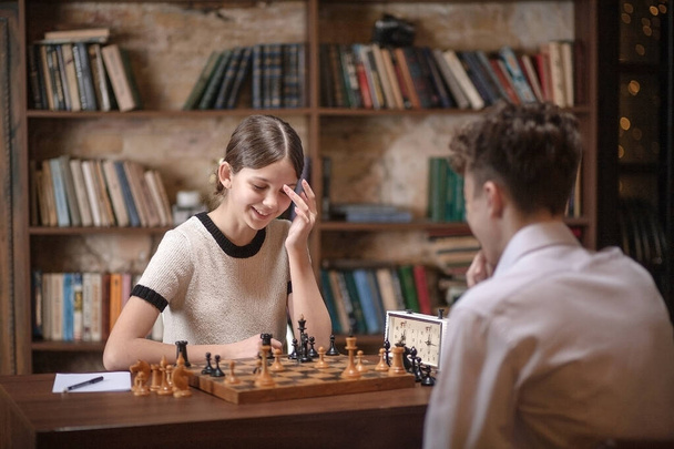 Un niño y una niña juegan ajedrez, los adolescentes juegan un juego de mesa, interés deportivo, los escolares están sentados en la mesa, aprendiendo a jugar ajedrez. - Foto, Imagen