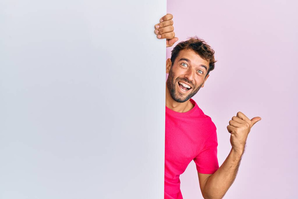Красивий чоловік з бородою тримає порожній банер, вказуючи великий палець в сторону посміхаючись щасливий з відкритим ротом
  - Фото, зображення