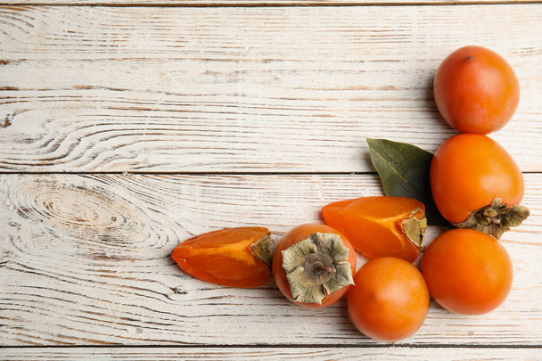 Delicious fresh persimmons on white wooden table, flat lay. Space for text - Foto, Imagem