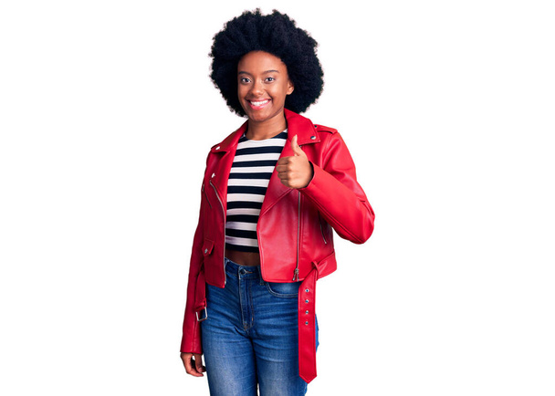 Giovane donna afroamericana con indosso giacca di pelle rossa sorridente felice e positivo, pollice in su facendo eccellente e segno di approvazione  - Foto, immagini