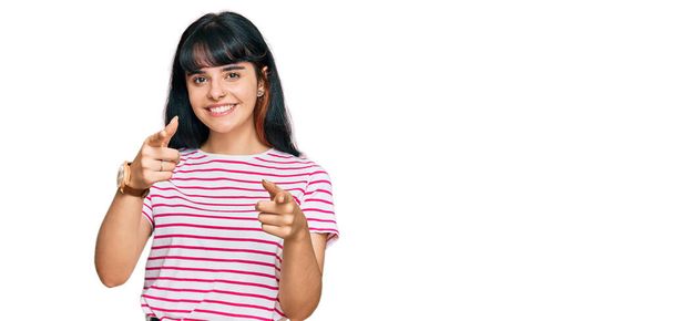 若いヒスパニック系の女の子が幸せと面白い顔でカメラに指を指してカジュアルな服を着て。良いエネルギーと振動は.  - 写真・画像
