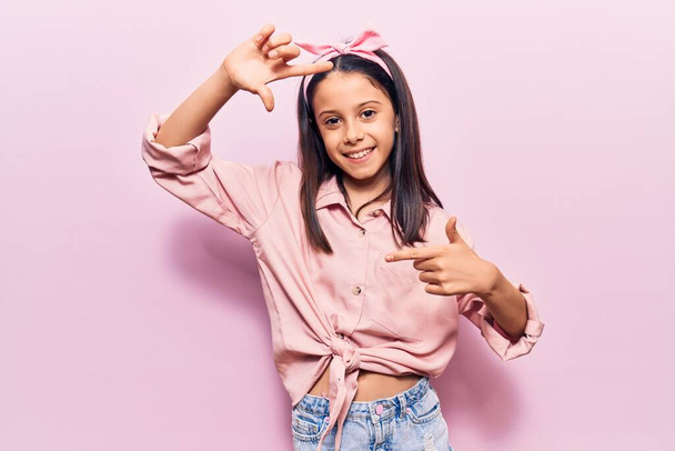 Beautiful child girl wearing casual clothes smiling making frame with hands and fingers with happy face. creativity and photography concept.  - Фото, зображення
