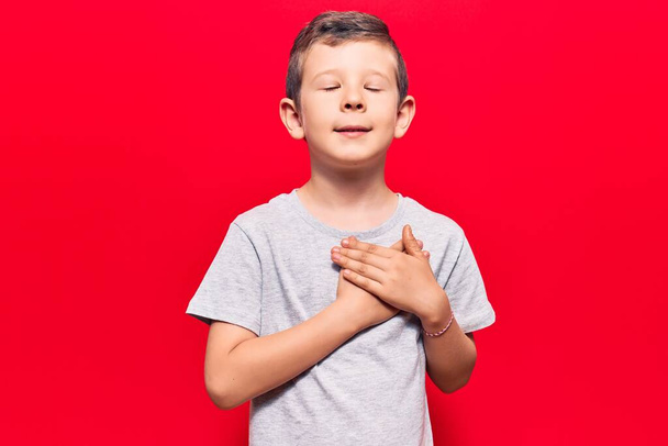 Cute blond kid wearing casual clothes smiling with hands on chest with closed eyes and grateful gesture on face. health concept.  - Fotografie, Obrázek