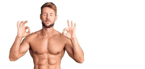 Young caucasian man standing shirtless relax and smiling with eyes closed doing meditation gesture with fingers. yoga concept.  - Valokuva, kuva