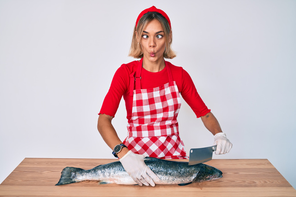 Bella donna caucasica pescivendolo che vende salmone crudo fresco facendo faccia di pesce con bocca e occhi strabici, pazzo e comico.  - Foto, immagini