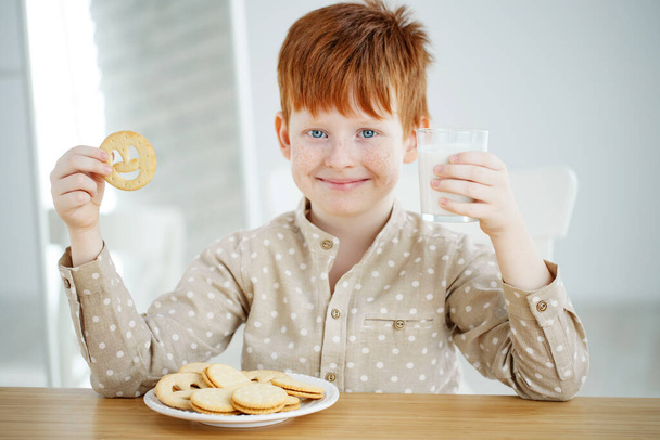 子供は朝食をとっている。子供は牛乳を飲み、クッキーを食べる。子供たちは晴れた朝に食べる。若い子供のための健康的なバランスの取れた栄養. - 写真・画像
