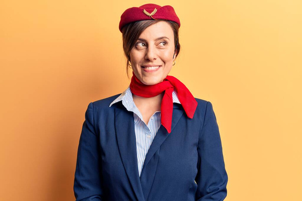 Młoda piękna kobieta w mundurze stewardessy uśmiecha się patrząc w bok i patrząc myśląc.  - Zdjęcie, obraz