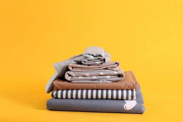 Stack of clean bed sheets on yellow background - Фото, зображення