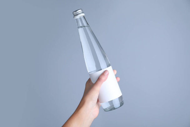 Woman holding glass bottle with soda water on light grey background, closeup - Foto, afbeelding