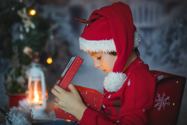 Cute child, school boy, opening present for christmas, decoration around him, outdoor shot, outdoor snow shot - Photo, Image