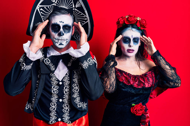 Young couple wearing mexican day of the dead costume over red with hand on head for pain in head because stress. suffering migraine.  - Fotoğraf, Görsel