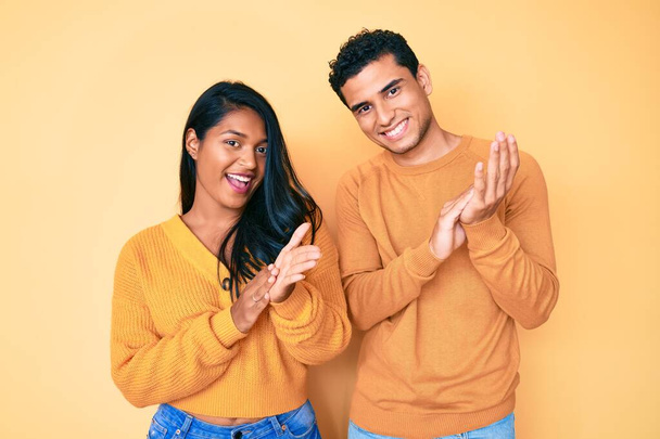 Beautiful latin young couple wearing casual clothes together clapping and applauding happy and joyful, smiling proud hands together  - Photo, Image