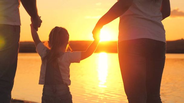 Little daughter jumping holding hands of dad and mom at sunset. Happy family life concept. A child with his parents plays together in flight. Mother and father on a walk with the kid. Spend the - Photo, Image