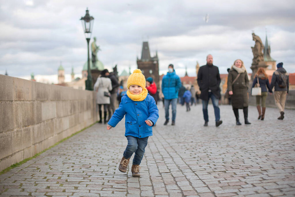 Cute child, boy with family, having a walk in Prague on Charles bridge wintertime - Foto, afbeelding