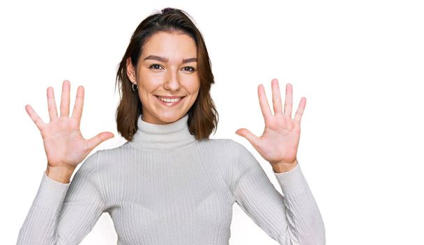 Fiatal kaukázusi lány alkalmi ruhát visel, mutatva és mutogatva a tízes számú ujjaival, miközben magabiztosan és boldogan mosolyog..  - Fotó, kép