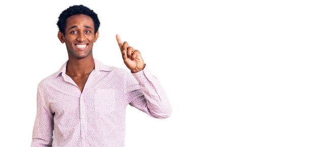Afričan pohledný muž na sobě ležérní růžová košile ukazující a ukazující nahoru s prstem číslo jedna při úsměvu sebevědomý a šťastný.  - Fotografie, Obrázek