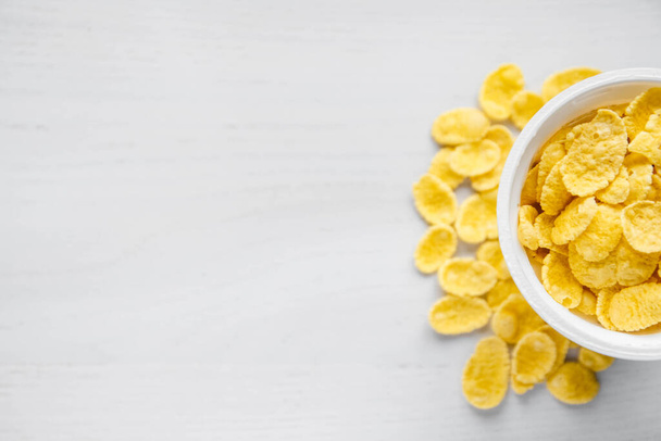 Cornflakes in white bowl on white wooden background. Top view. Copy, empty space for text. - Photo, Image