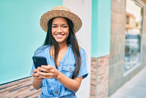 Молодая латинская туристка в отпуске улыбается счастливой, используя смартфон в городе. - Фото, изображение