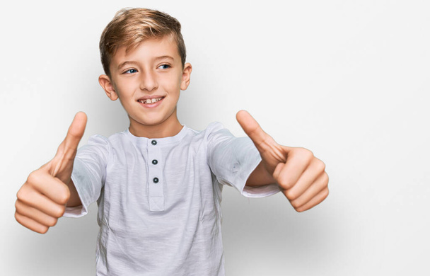 Petit garçon caucasien portant des vêtements décontractés approuvant faire un geste positif avec la main, pouces levés souriant et heureux pour le succès. geste gagnant.  - Photo, image