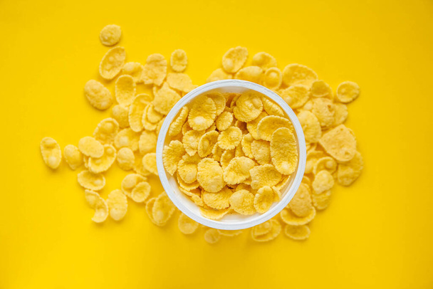 Cornflakes in white bowl on yellow background. Top view. Copy, empty space for text. - Foto, imagen