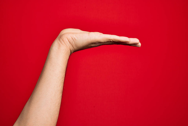 Hand of caucasian young man showing fingers over isolated red background with flat palm presenting product, offer and giving gesture, blank copy space - Φωτογραφία, εικόνα