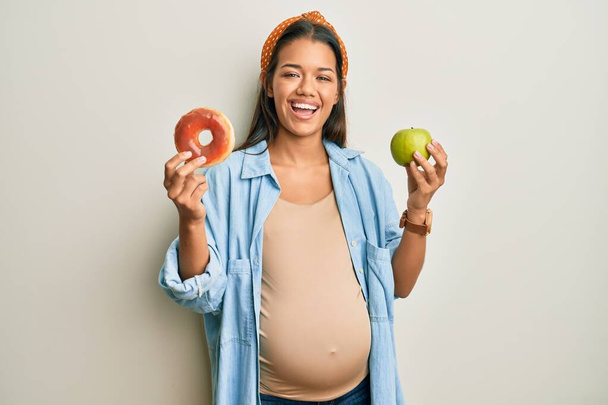 Belle femme hispanique attendant un bébé, tenant la nourriture souriante et riant fort à haute voix parce que drôle blague folle.  - Photo, image