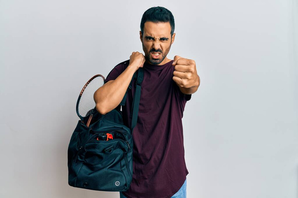 Young hispanic man holding gym bag annoyed and frustrated shouting with anger, yelling crazy with anger and hand raised  - Fotografie, Obrázek