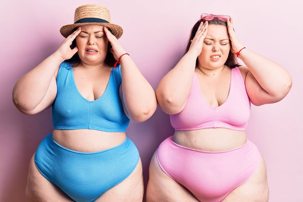Young plus size twins wearing bikini suffering from headache desperate and stressed because pain and migraine. hands on head.  - 写真・画像