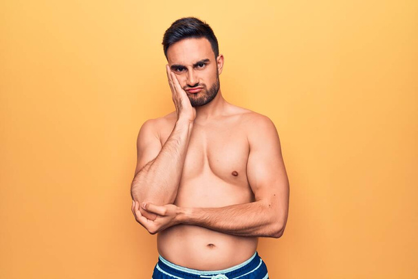 Young handsome man with beard wearing sleeveless t-shirt standing over yellow background thinking looking tired and bored with depression problems with crossed arms. - Photo, Image