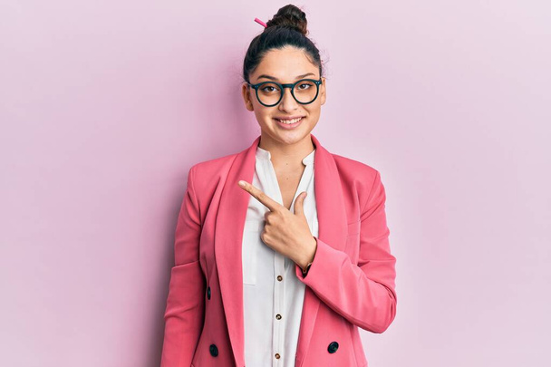 Beautiful middle eastern woman wearing business jacket and glasses cheerful with a smile on face pointing with hand and finger up to the side with happy and natural expression  - Photo, Image