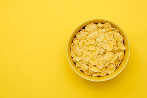 Cornflakes in yellow bowl on yellow background for cereal healthy food. Top view. Copy, empty space for text. - Foto, afbeelding