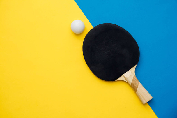 Tafeltennis of ping pong racket en bal op blauwe en gele achtergrond. Bovenaanzicht. Kopieer, lege ruimte voor tekst. - Foto, afbeelding