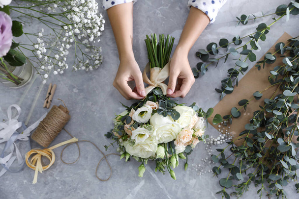 Florist tieing bow on beautiful wedding bouquet at light grey marble table, top view - Photo, image