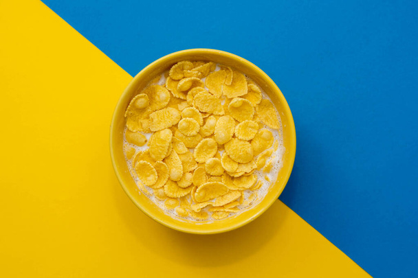 Cornflakes with milk in the yellow bowl on blue and yellow background. Top view. Copy, empty space for text. - Photo, Image