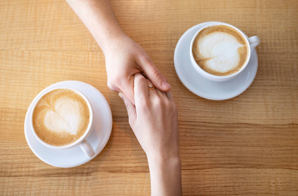 Vista da vicino della coppia millenaria che si tiene per mano mentre prende un caffè a tavola nel caffè - Foto, immagini
