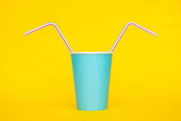 Blue paper cup with drinking colored plastic straws on yellow background. Set for party. Minimalist Style. Copy, empty space for text. - Foto, imagen