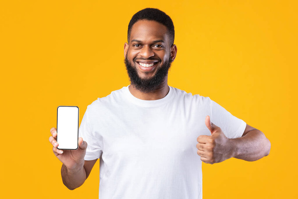 African Guy Showing Smartphone Blank Screen Gesturing Thumbs-Up, Yellow Background - Foto, imagen
