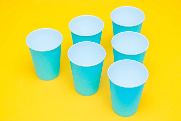 Blue paper disposable cups on yellow background. Set for party. Top view. Minimalist Style. Copy, empty space for text. - Фото, зображення