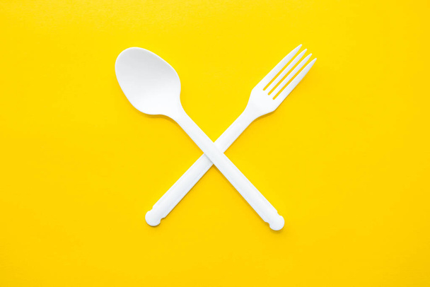 Forchetta incrociata in plastica bianca e cucchiaio su fondo giallo. Utensile da cucina. Segno di posate. Vista dall'alto. Stile minimalista. Copia, spazio vuoto per il testo. - Foto, immagini
