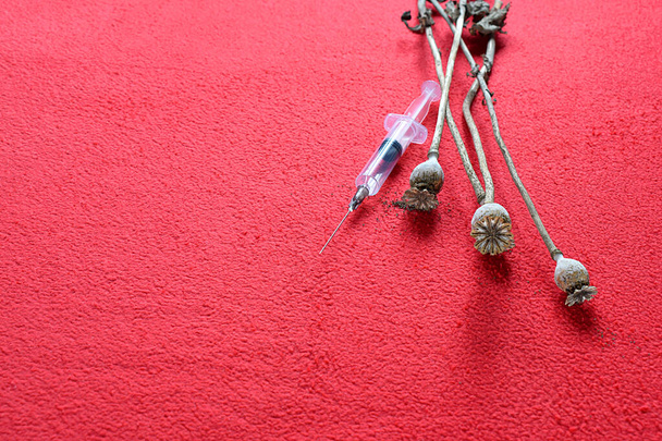 Capsules de graines de pavot et seringue jetable sur fond rouge. - Photo, image
