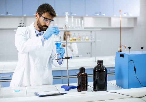 Guapo joven investigador que trabaja con líquido azul en vidrio de laboratorio en el laboratorio - Foto, Imagen