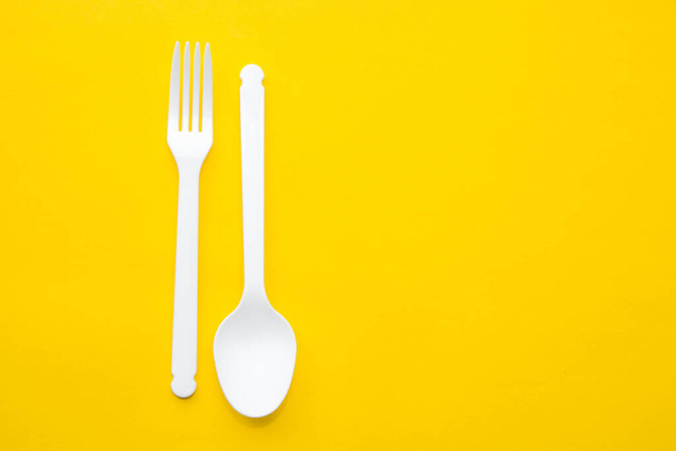Plastic white spoon and fork on yellow background. Cooking utensil. Cutlery sign. Top view. Minimalist Style. Copy, empty space for text. - Foto, immagini