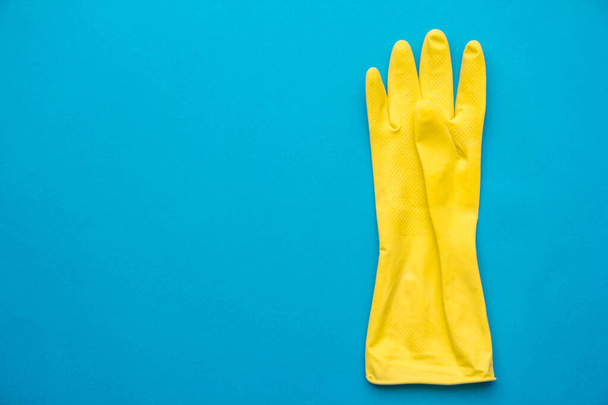 Žlutá gumová rukavice pro čištění visí na modrém pozadí. Horní pohled. Minimalistický styl. Kopírovat, prázdné místo pro text. - Fotografie, Obrázek
