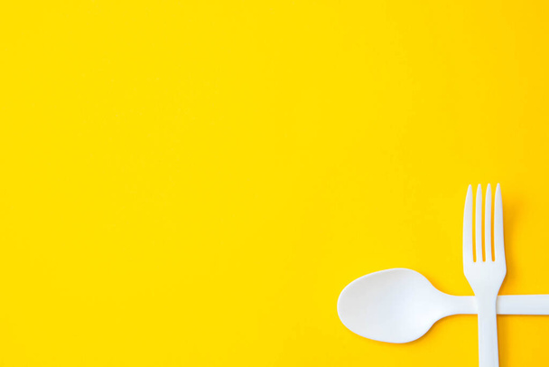 Plastic white crossed fork and spoon on on yellow background. Cooking utensil. Cutlery sign. Top view. Minimalist Style. Copy, empty space for text. - Foto, imagen