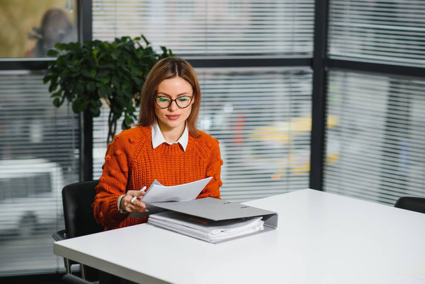 Portrait of a happy casual businesswoman in sweater sitting at her workplace in office - Фото, зображення