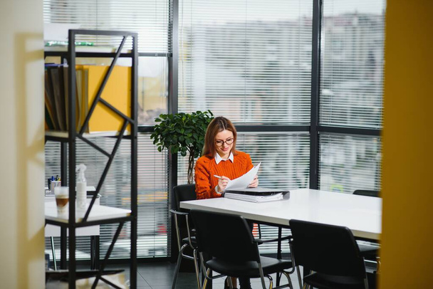 Portrait of a happy casual businesswoman in sweater sitting at her workplace in office - Valokuva, kuva