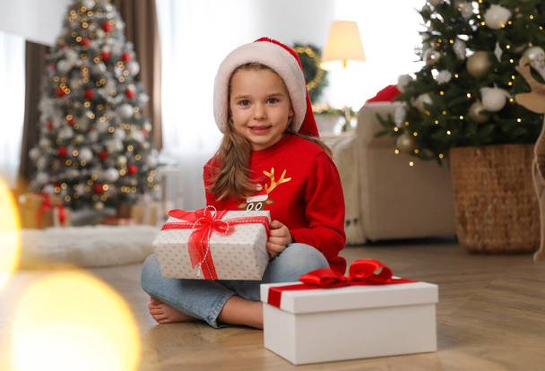 Cute little girl holding gift box in room decorated for Christmas - Fotó, kép