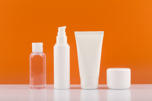 Set of skincare cosmetics on white glossy table against orange background. Concept of skincare and wellbeing - Foto, Imagem